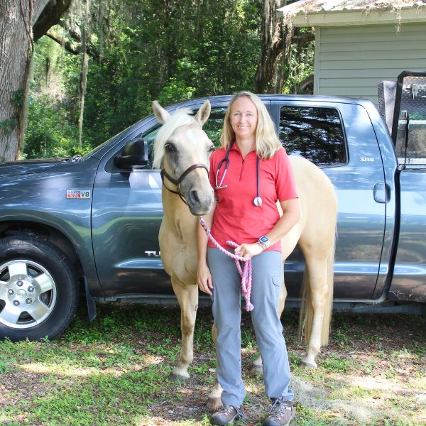 A woman in a red shirt stands beside a horse